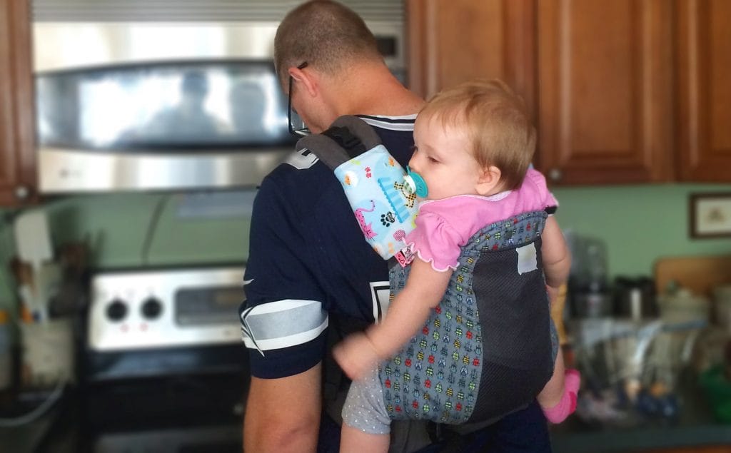 Dad faces stove, cooking, while wearing toddler in carrier on his back