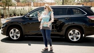 Mom standing outside with baby in baby carrier looking at YourMechanic app