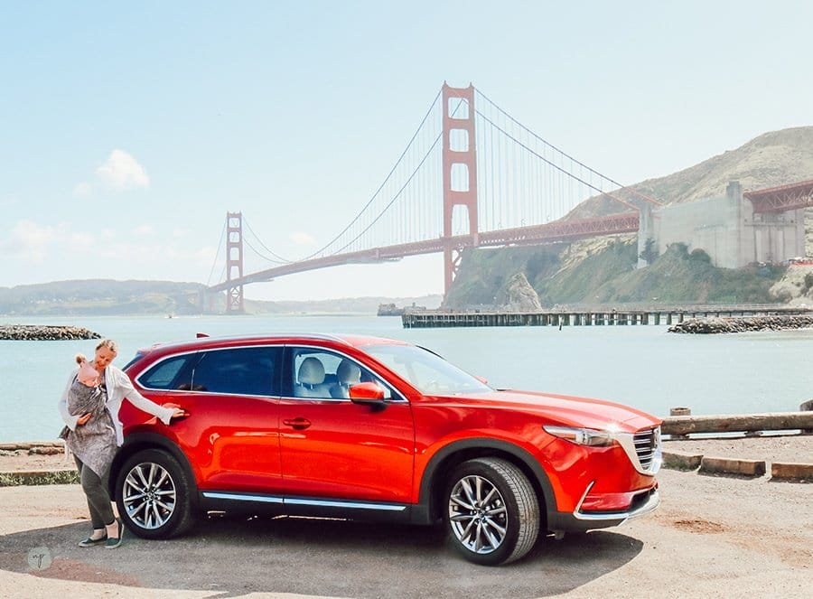 mom and baby standing by open door of a Mazda CX-9 in SF with Golden Gate Bridge in the background