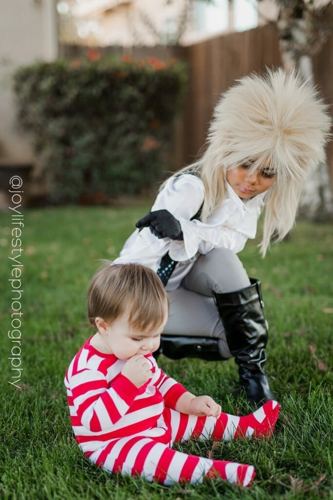 Little girl dressed as Labyrinth king character bends down to reach baby brother