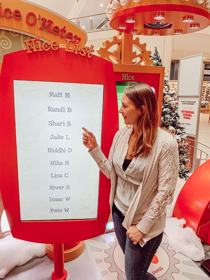 Woman (Shari) pointing at a monitor called the "Nice List" with a list of names on it to show that she's on the list