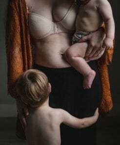 postpartum mom with baby on hip and toddler hugging her legs