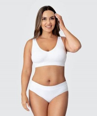 woman stands facing camera with left hand in her hair wearing white shapermint bra and panties