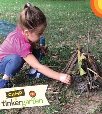 Toddler girl in jeans and pink shirt makes a camp fire with sticks outsie