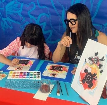 mom looks over at daughter's painting work at art table