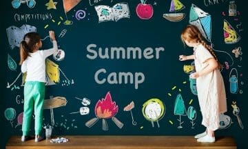 two girls color on a chalkboard that says "summer camp"