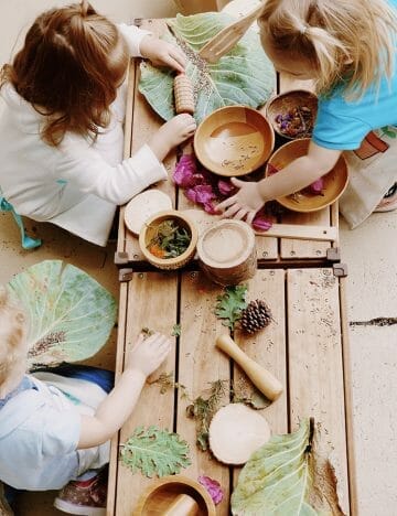 children sit around wooden table with wooden bowls and leaves