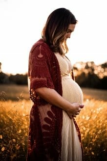 Pregnant woman holds belly while standing in wheat field