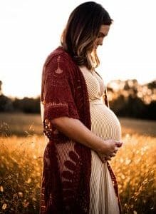 Pregnant woman holds belly while standing in wheat field