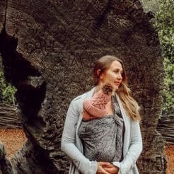 babywearing mom holds baby near tree trunk