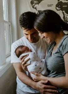 new postpartum parents hold swaddled newborn in their arms and smile