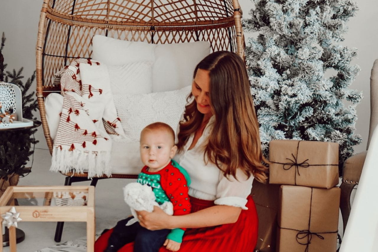 mom sits with baby near Christmas tree and all of the baby holiday gifts