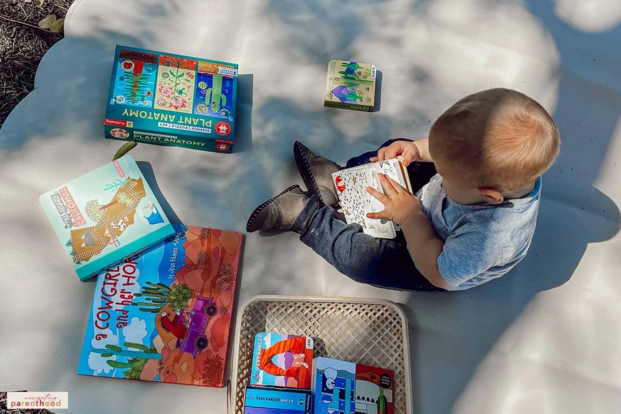 one-year-old boy looks at Mudbuppy brand books on a Wander & Roam vegan leather mat at his Wild West first birthday party